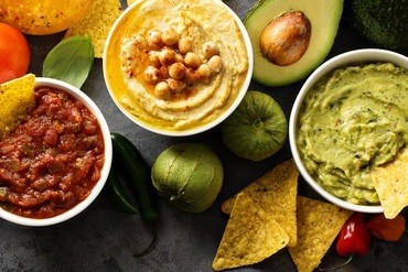 Homemade hummus, salsa and guacamole with corn chips Homemade hummus, salsa and guacamole with corn chips and vegetables overhead view